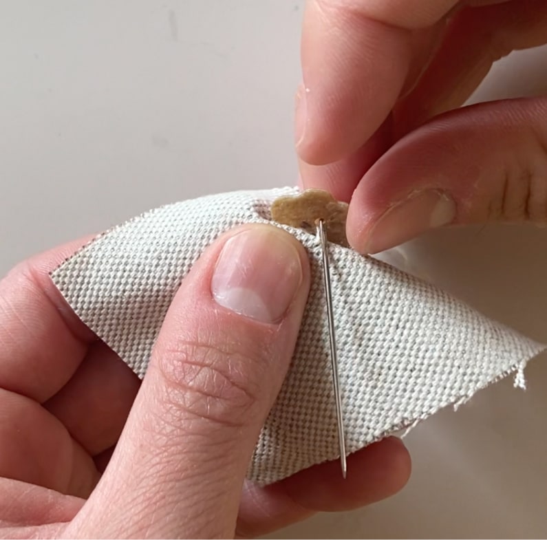 Une couturière passe dans les trous du bouton une dernière fois, sans piquer dans le tissu.