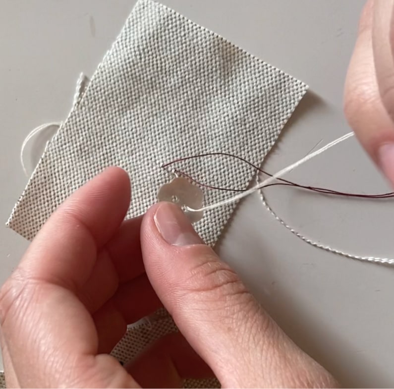 Une couturière enfile l'aiguille dans un des trous du bouton.