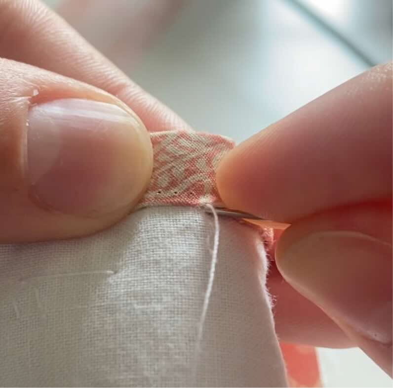 Une couturière pique en face du biais sur l'envers de la couverture pour coudre le biais à la main.