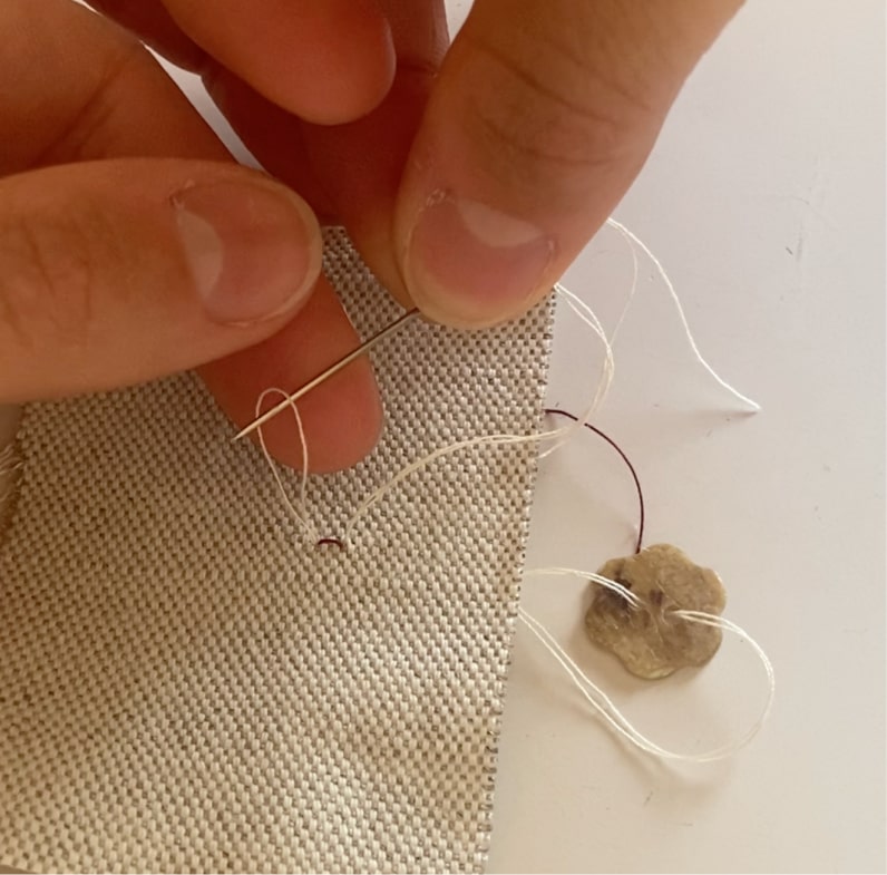 Une couturière passe l'aiguille dans la boucle du fil à l'arrière du coupon pour réaliser un point d'arrêt.