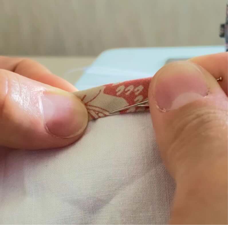 Une couturière épingle le bord du biais à l'envers de la couverture.