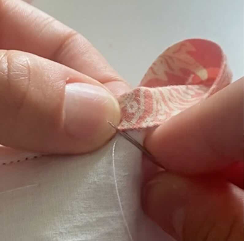 Une couturière pique dans l'extrémité du pli du biais pour coudre le biais à main.