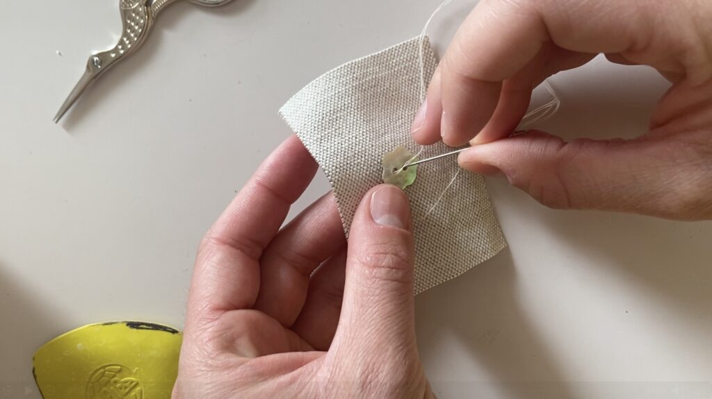 Une couturière coud un bouton nacré sur un coupon de tissus beige.