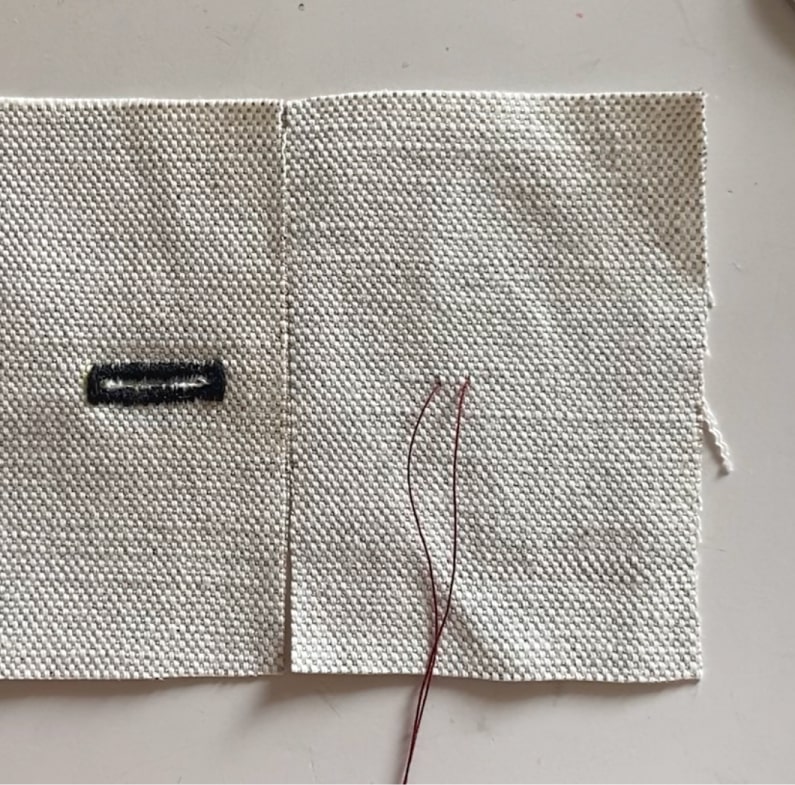 Des fils colorés marquent l'emplacement du bouton sur un coupon de tissu.