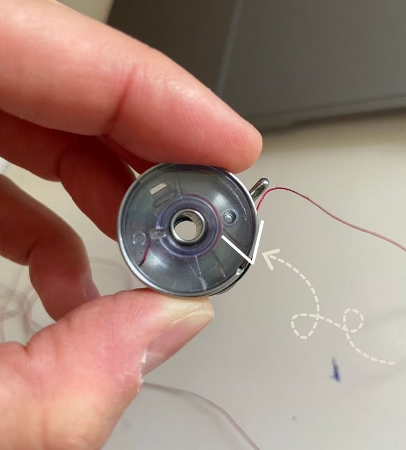 Canette insérée dans le support de canette de telle sorte que le fil forme un V qui va du centre de la canette jusqu'à l'extrémité qui sort du support.